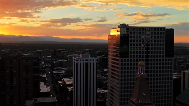 Close orbit around the top of the Daniels and Fisher Tower and flag, pulling back to reveal a sunset sky over Denver with the Rocky Mountains silhouetted in the distance.