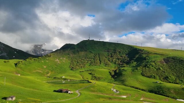 Picturesque summer panorama of Metschstand in Lenk, Switzerland, featuring Speichersee Brenggen, alpine chalets, and sweeping Swiss Alps under a partly cloudy sky with dramatic cloud shadows