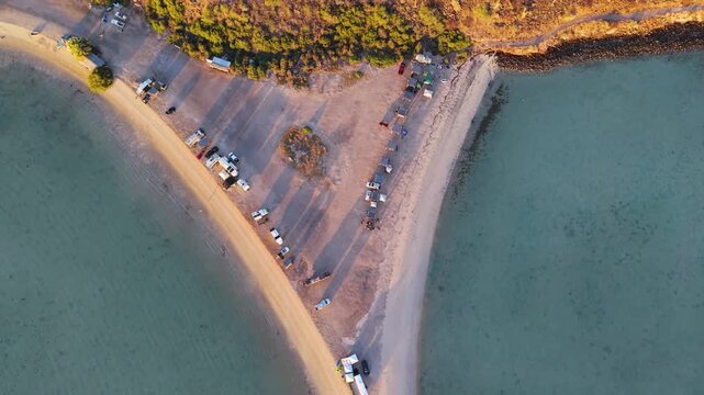 A striking 90-degree aerial top-down sequence framing camper vans, overlander trucks, and RVs parked along the symmetrical sand split of Playa El Reques&oacute;n.