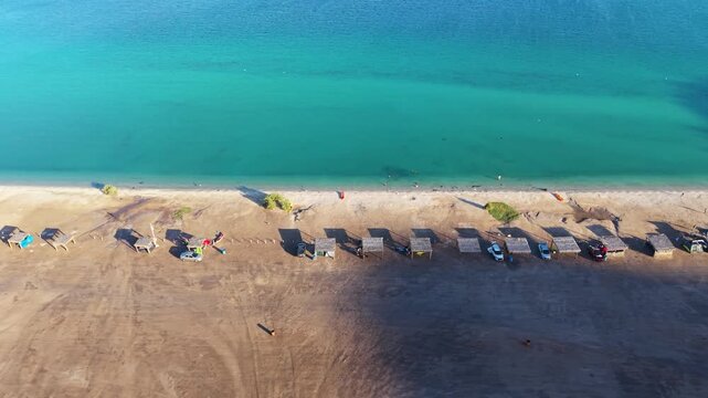 A striking high-angle aerial view of traditional thatched-roof palapas and camper setups lined symmetrically along the calm turquoise shores of Bah&iacute;a Concepci&oacute;n.