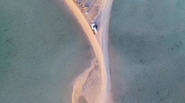 A striking 90-degree top-down drone sequence framing camper vans and overlanding setups along a narrow, symmetrical desert sandspit.