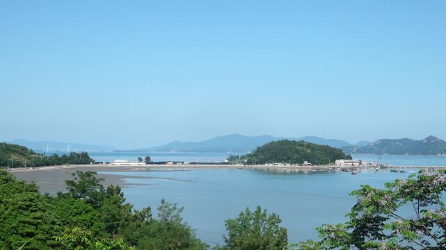 Scenic view of a peaceful Korean southern sea fishing village with local fisherman boats, mudflats, and islands in Namhae / 한국 남해바다 어촌 마을 풍경, 어민들의 고기잡이 배와 평화로운 섬, 갯벌 해안가 풍경 영상