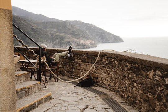 Traveler relaxing on a terrace overlooking a scenic Mediterranean coastline, enjoying a peaceful mountain and sea view in Cinque Terre, Italy.