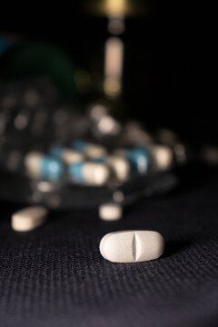 Single white tablet with blurred blister pack.White tablets and capsules scattered on a dark surface with blister packs in soft focus, showing medicine, treatment, healthcare, and prescript