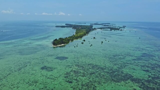 Aerial view of a tropical island archipelago surrounded by clear turquoise sea and coral reefs. Drone shot of an island strip with green trees in the ocean. Pari island in Indonesia 