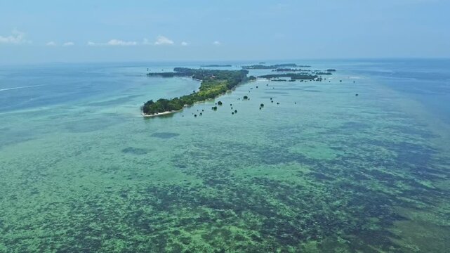Aerial view of a tropical island archipelago surrounded by clear turquoise sea and coral reefs. Drone shot of an island strip with green trees in the ocean. Pari island in Indonesia 