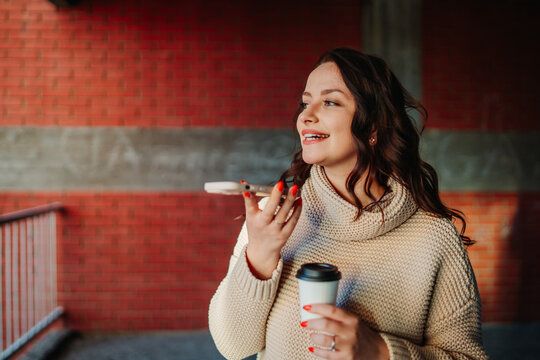 Woman sending voice message on smartphone holding coffee