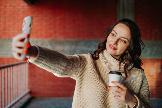 Woman taking selfie with smartphone holding coffee cup