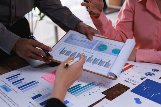 Business professionals analyzing financial data and market growth charts, collaborating on a digital marketing strategy, and planning economic development at an office meeting