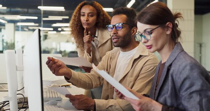 Coworkers in an office meeting review analysis. Focused professionals review documents at the monitor to improve planning, strategy and productivity. Strong teamwork and collaboration concept.