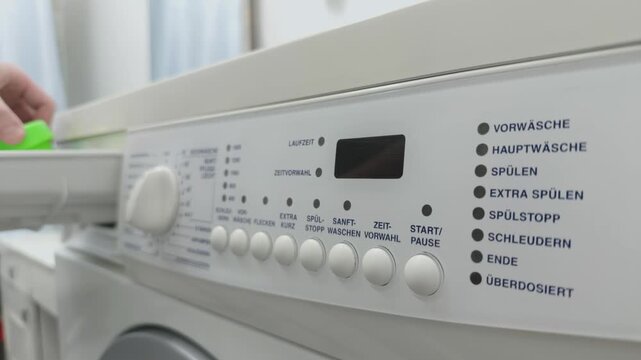 Close-up of a person's hand pouring detergent and turning on a washing machine, selecting a program mode and pressing the "Start" button on the control panel.