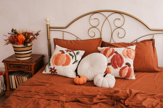 Decorative bed with orange and white pillows featuring pumpkin designs in a cozy room setting during autumn