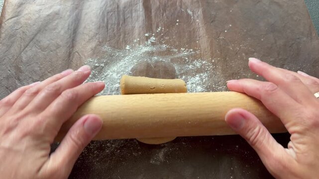 hands flattening and stretching dough on a floured silicone baking mat in natural light. homemade baking and pastry preparation.