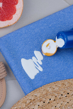 Close-up of white sunscreen lotion spilled from a blue bottle onto blue fabric with summer accessories nearby. Concept cosmetic stains on the cloth. top view
