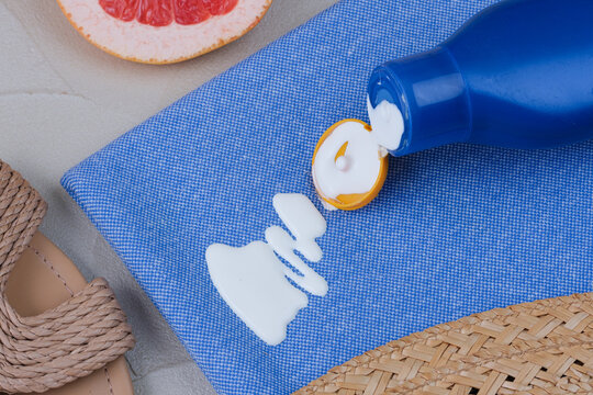 Close-up of white sunscreen lotion spilled from a blue bottle onto blue fabric with summer accessories nearby. Concept cosmetic stains on the cloth. top view