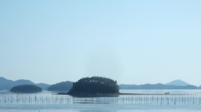 Scenic view of a peaceful Korean southern sea fishing village with local fisherman boats, mudflats, and islands in Namhae / 한국 남해바다 어촌 마을 풍경, 어민들의 고기잡이 배와 평화로운 섬, 갯벌 해안가 풍경 영상