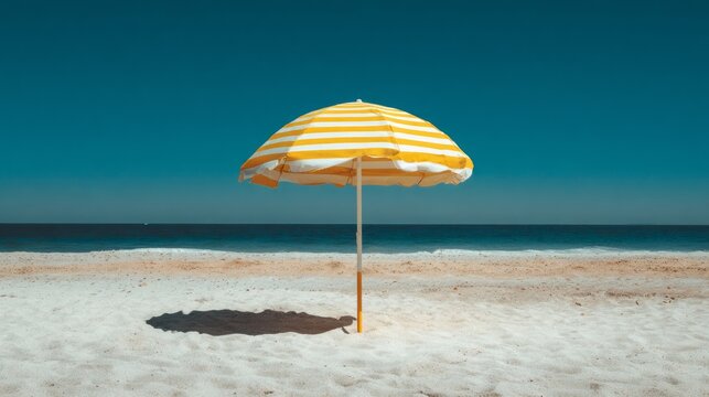 Large yellow and white striped beach umbrella providing shade on sandy shoreline with blue ocean, sunny summer vacation destination, tropical coastal landscape, seaside relaxation, travel and leisure 
