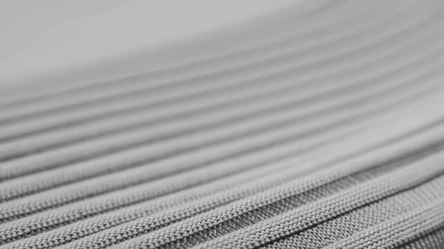 Diagonal close-up of braided textile cords with soft directional light, shallow focus, tight knit loops, ribbed texture, layered strands, repeating pattern, and subtle monochrome contrast
