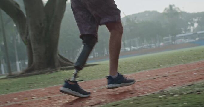Low angle view of a runner with a lower limb prosthesis jogging around an outdoor track, showcasing adaptive sport, cardiovascular fitness,