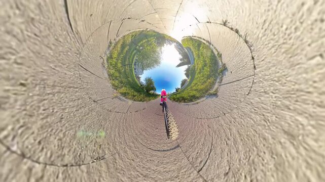 Cycling tiny planet adventure, person rides bicycle on paved park path in sunny outdoor scene with unique spherical distortion.