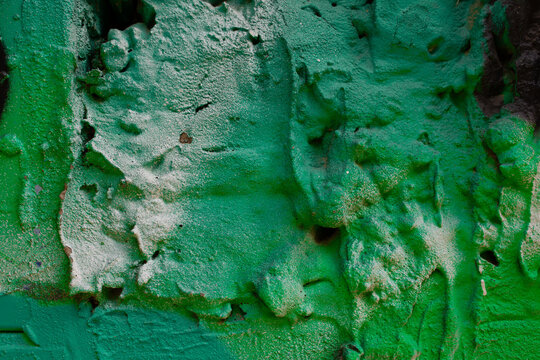 Cracked green paint peeling off a weathered textured wall surface