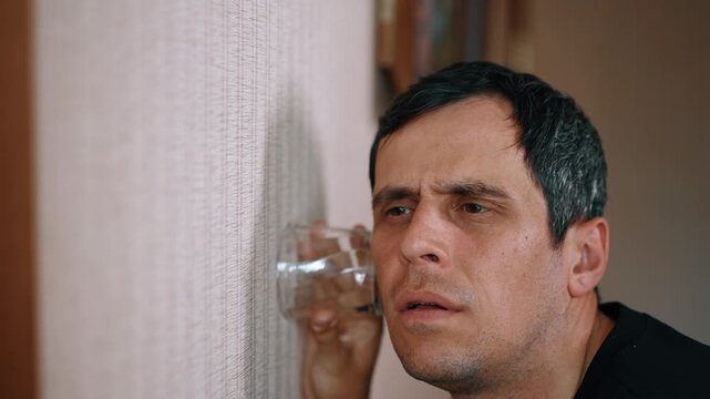 Curious man pressing a glass cup to a wall to eavesdrop on neighbors