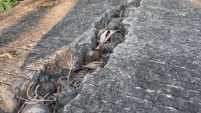 Wide fissure on damaged concrete road filled with stones
