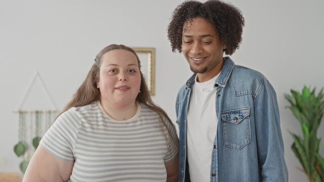 Man and plus size woman stand close, smiling faces, man in denim jacket and woman in striped shirt inside a bright building; joy togetherness.