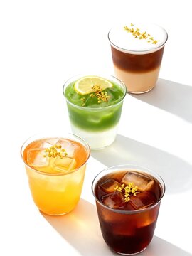 Four different iced cold drinks in clear glasses with ice cubes decorated with golden osmanthus flowers on plain white background showing refreshing summer beverage concept