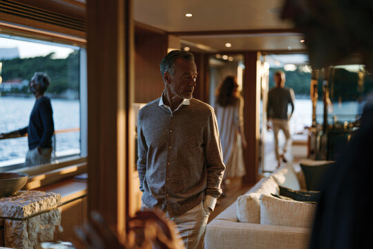 The image captures a classy man appreciating the scenic ambiance of a luxurious yacht, surrounded by beautiful friends and the serene seaside, evoking comfort and joy.