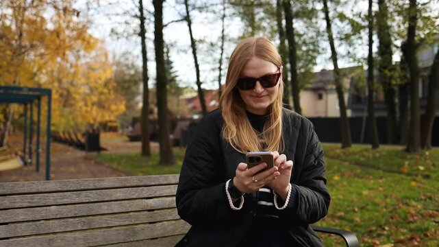 Close up of a young female holding and using mobile phone outdoors against green nature background