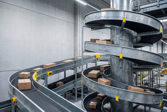 Cardboard boxes move along a spiral conveyor system inside a modern automated distribution warehouse.