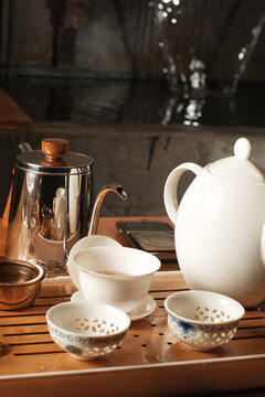 Traditional Chinese gongfu tea set with a white ceramic teapot, gaiwan, patterned cups, and a metallic kettle arranged on a wooden tea tray.