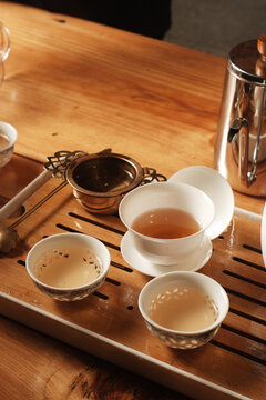 Traditional Chinese tea ceremony set with porcelain cups filled with warm tea on a wooden bamboo tray.