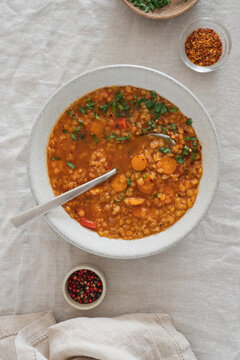 Hearty lentil soup served in a rustic bowl on a natural linen tablecloth. High protein comfort food concept featuring fiber-rich legumes, wholesome ingredients and nourishing homemade meal