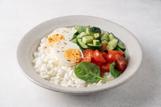 Fresh high protein savory cottage cheese bowl with cherry tomatoes, cucumber, boiled egg and chili flakes served on light background with copy space.
