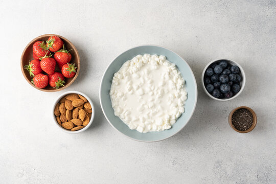 Fresh ingredients for a high protein cottage cheese bowl including blueberries, strawberries, chia seeds and almonds arranged on a light background with copy space