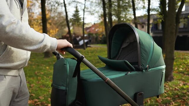 a person is casually pushing a stroller through a park or garden area, surrounded by greenery and trees. the relaxed and casual atmosphere reflects a family life and parenting scene, ideal.
