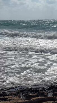 Rough sea waves breaking on the Cyprus coast during a red flag warning, unsafe swimming conditions, beach safety, coastal hazard, dangerous weather, travel risk.