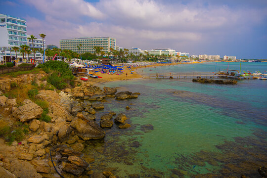 View on Protaras (Paralimni) sand beach with hotels, promenade, tourists, umbrellas, sunbeds near Mediterranean seashore, Cyprus
