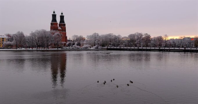 Klosters Church in Eskilstuna, Sweden in winter morning, with its brick twin towers and rime-covered trees perfectly reflecting on Eskilstuna river water surface.