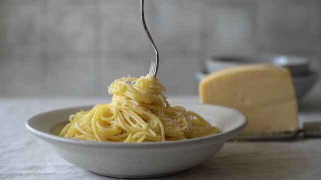 Close-up video of a hand twirling cheesy pasta on a fork above a plate of freshly prepared spaghetti. Authentic Italian comfort food scene featuring melted cheese, rich texture and appetizing pasta st