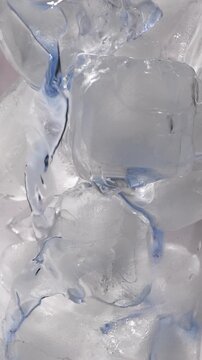 Vertical macro video of vibrant blue butterfly pea tea flowing smoothly ice cubes in a transparent glass. Captured in slow motion, highlighting the elegant movement of the liquid and the refreshing ap