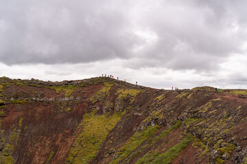 People walking along the rim of a red volcanic crater covered with green moss, Iceland © ThinDepthMacro