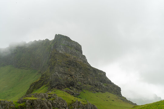 Rocky green mountain peak shrouded in low cloud and mist, Iceland