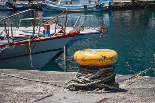Thick weathered ropes (mooring lines) coiled around yellow bollard for mooring fishing boat at Keelung harbour, Taiwan, traditional maritime industry equipments used in local coastal fisherman culture