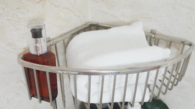 Reducing visual clutter. Bathroom corner shelf rack providing organized storage for personal hygiene products, including folded clean white towels and a dispenser