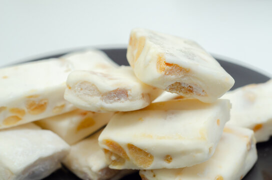 White nougat bars with nut pieces rest on a dark plate