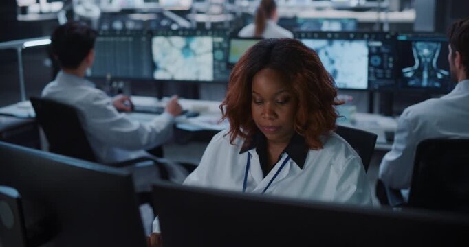 Portrait of Black Female Scientist Analyzes MRI Scans and Molecular Data on Multiple Monitors in a Modern Medical Lab, While Colleagues Works Nearby, Using AI for Drug Research and Diagnosis.