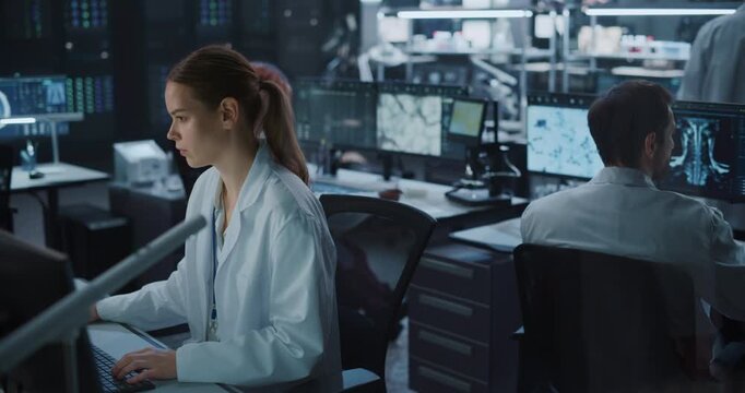Portrait of White Female Scientist in White Lab Coat Types on Computer While Male Colleagues Study Spinal Scans and Molecular Data With Ai in a Dim, Modern Medical Research Laboratory.